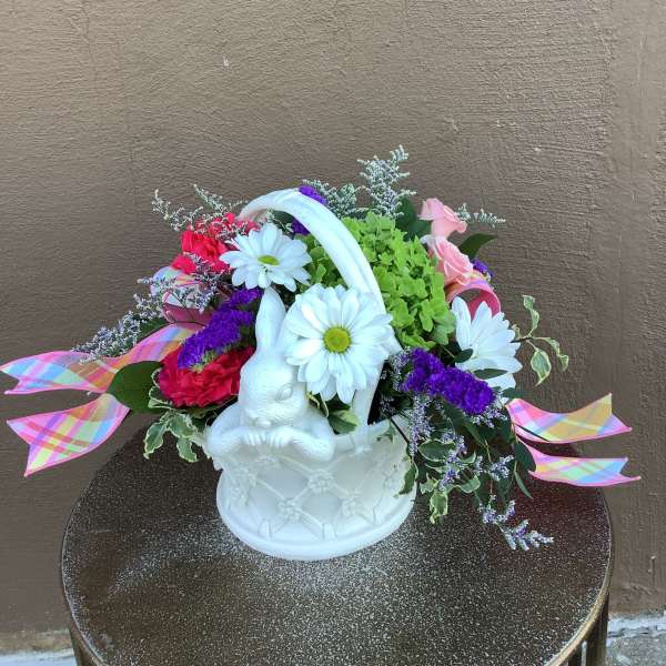 Pastel arrangement with daisies, roses, and carnations in a white bunny basket with plaid ribbons.
