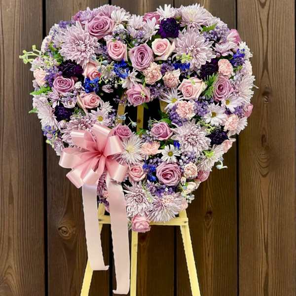 Heart-shaped standing wreath of pink and purple flowers with a large pink bow on a wooden easel