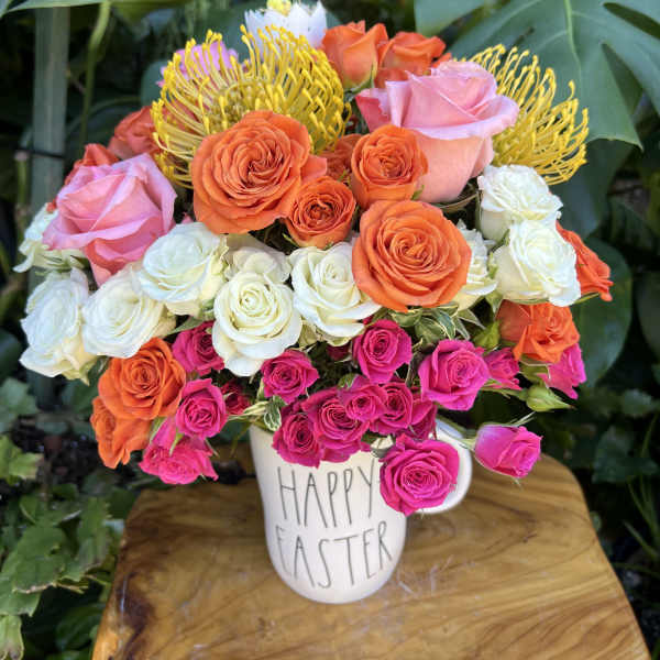 Colorful rose and protea arrangement in a 'Happy Easter' mug on a wooden surface
