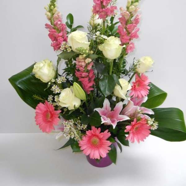 Tall arrangement of pink snapdragons, gerbera daisies, lilies, and white roses in a purple pot