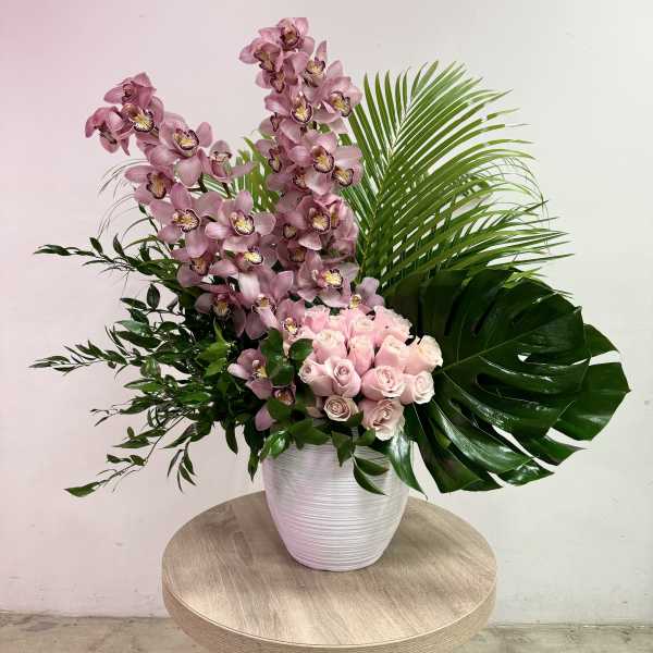 Large pink orchid and rose arrangement in a white vase on a small table