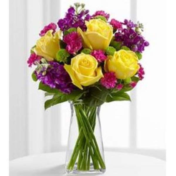 Tall glass vase with yellow roses, purple and pink blooms, and green accents
