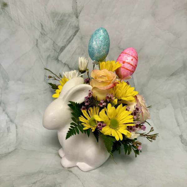 White bunny vase with yellow daisies, peach roses, and pastel decorative egg picks.