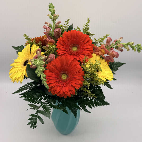 Bright red and yellow gerbera daisies with snapdragons in a teal vase
