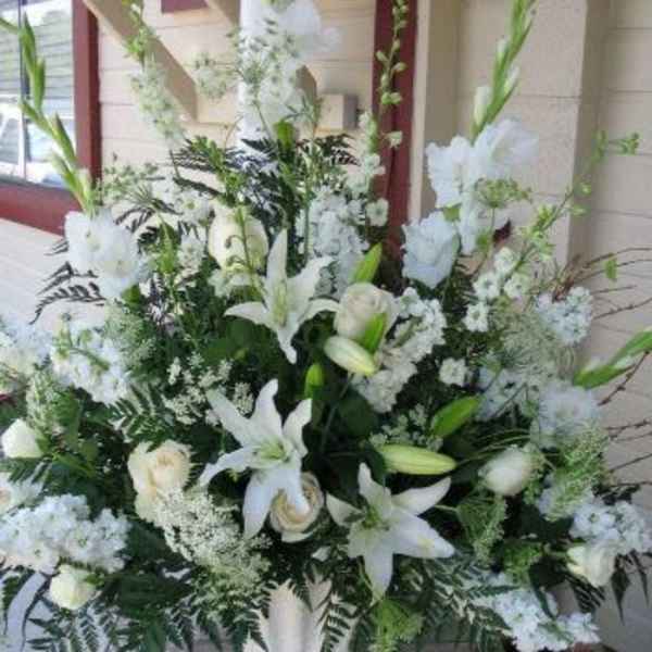 Tall all-white arrangement with lilies, roses, and snapdragons in a white pedestal vase