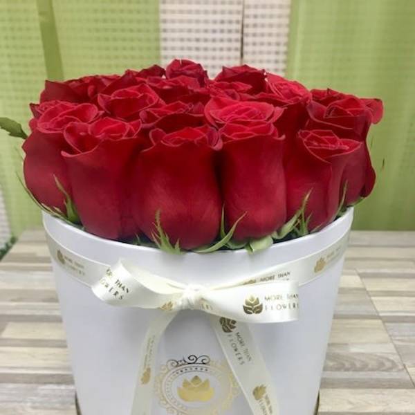 Round white hatbox filled with tightly packed red roses and tied with a cream ribbon bow.