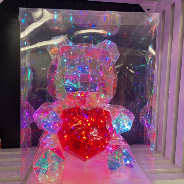 Faceted clear teddy bear figurine with multicolor lights holding a glowing red heart in a clear display box