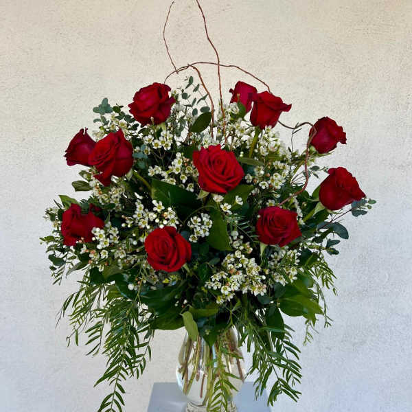 Arrangement of red roses with small white flowers and cascading greenery in a clear glass vase.