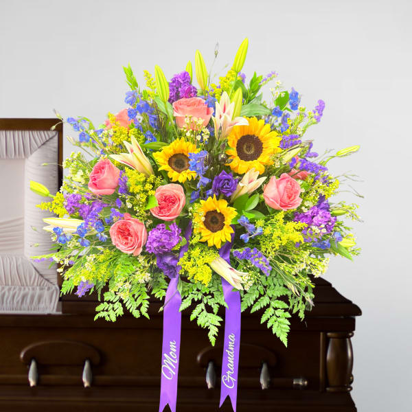 Bright casket spray with sunflowers, pink roses, lilies and purple blooms on a wooden casket