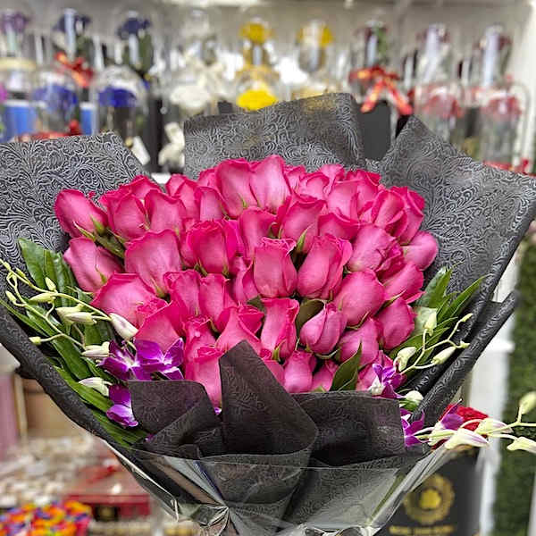 Large bouquet of bright pink roses with purple orchids wrapped in black paper.