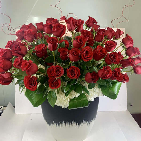 Large arrangement of red roses and white flowers in a black and white ceramic pot