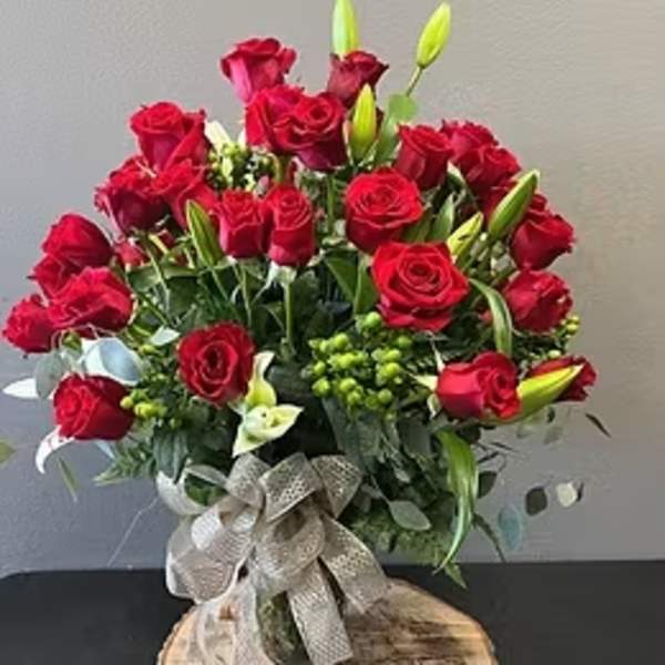 Large arrangement of red roses with white calla lilies and lily buds in a glass vase with burlap bow.