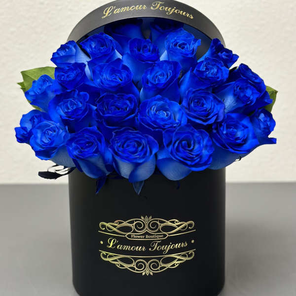 Round hatbox of vivid blue roses in a black cylinder container with gold script.