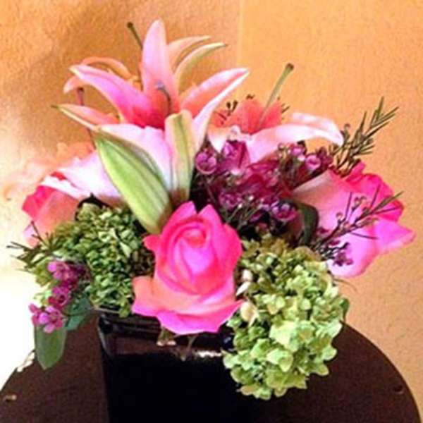 Compact arrangement of pink lilies and roses with green hydrangeas in a black square vase