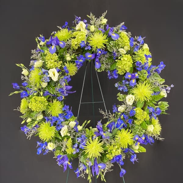 Standing wreath of bright green mums, blue delphinium and iris, and ivory blooms on a metal easel