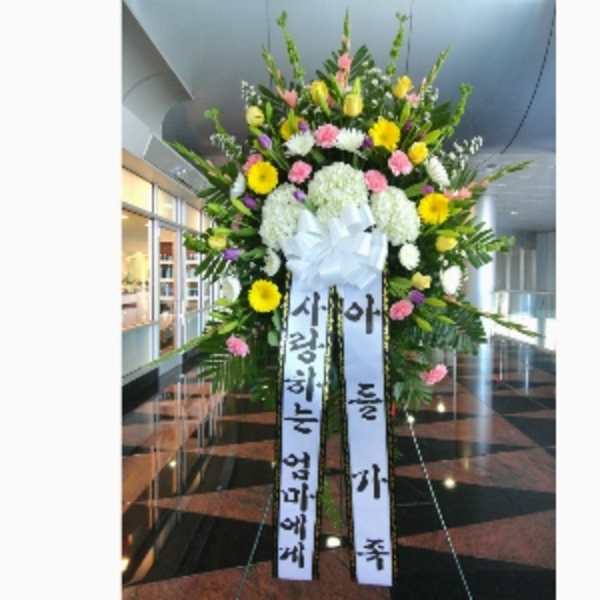 Tall standing sympathy spray with yellow, pink, and white flowers and Korean message ribbons on an easel