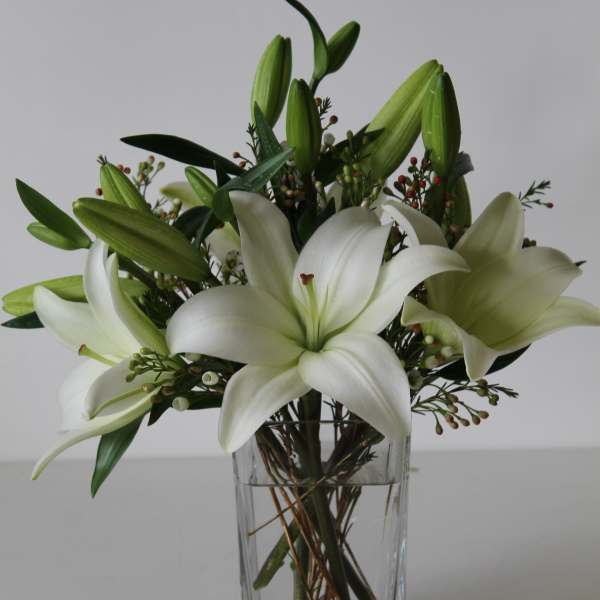 Arrangement of white lilies with green buds in a clear rectangular glass vase