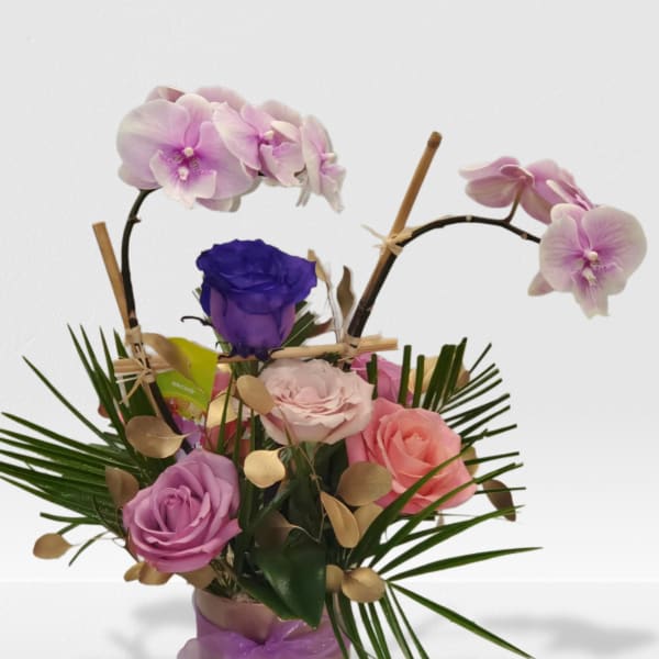 Arrangement of pink orchids and mixed roses in a cylinder vase with palm accents and a purple ribbon