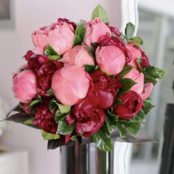 Round bouquet of pink and dark red peonies in a tall dark glass vase
