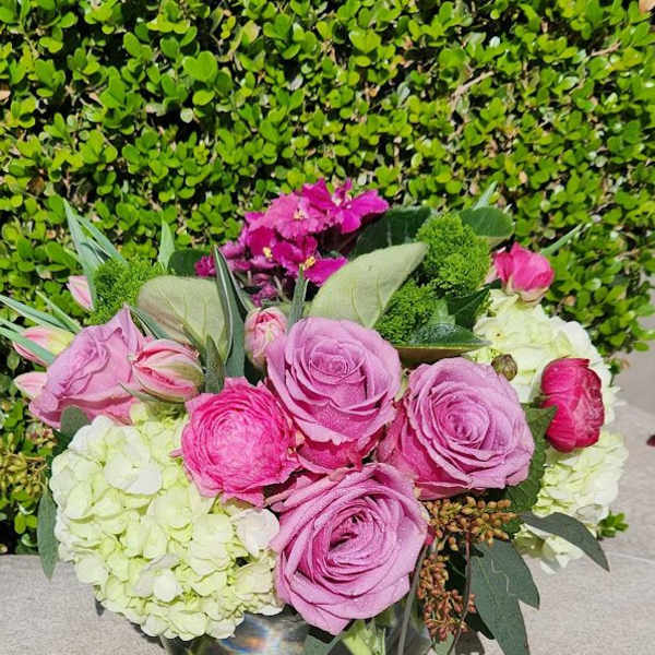 Low glass vase with pink roses, ranunculus, and green hydrangeas in a compact round bouquet