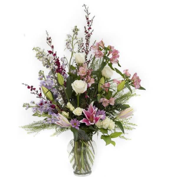Tall mixed arrangement of pink lilies, white roses, and lavender blooms in a clear glass vase