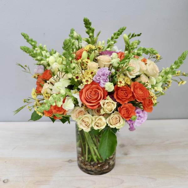 Vase arrangement of orange and cream roses with snapdragons and touches of yellow and lavender flowers