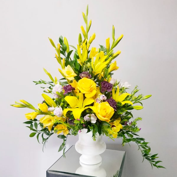 Tall yellow and purple flower arrangement in a white pedestal vase