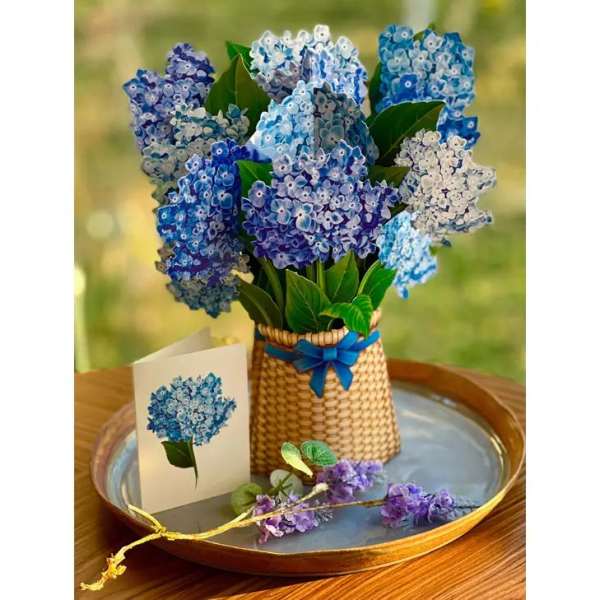 Blue and purple hydrangea-style silk flowers in a basket with matching card on a tray