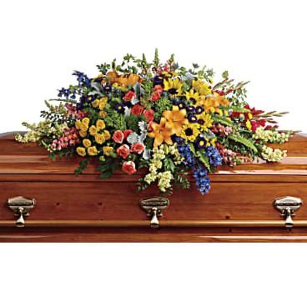 Large multicolor casket spray of mixed flowers arranged atop a wood coffin