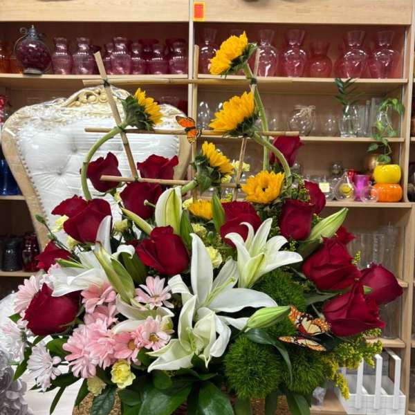 Basket arrangement of red roses, white lilies, sunflowers, and pink daisies with decorative butterflies