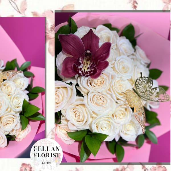 Round bouquet of cream roses with a burgundy orchid and gold butterfly picks in pink wrap.