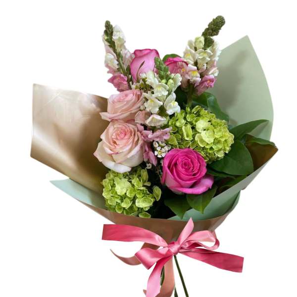 Hand-tied bouquet of pink roses, white snapdragons, and green hydrangeas wrapped in paper with a pink ribbon.