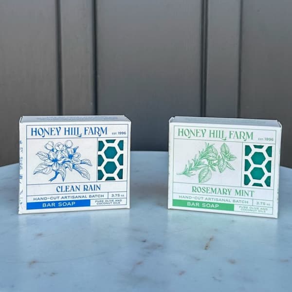 Two Honey Hill Farm bar soap boxes, Clean Rain and Rosemary Mint, on a light stone surface
