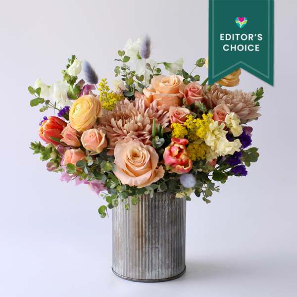 Peach roses, mums, ranunculus, and mixed blooms in a galvanized metal cylinder vase.
