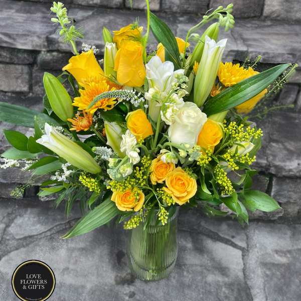 Tall yellow and white arrangement with roses and lilies in a clear glass vase
