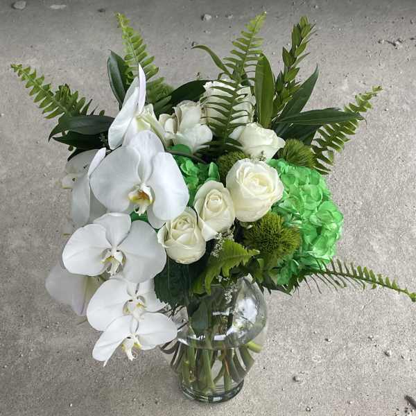 White orchids and roses in a glass vase with bright green hydrangea