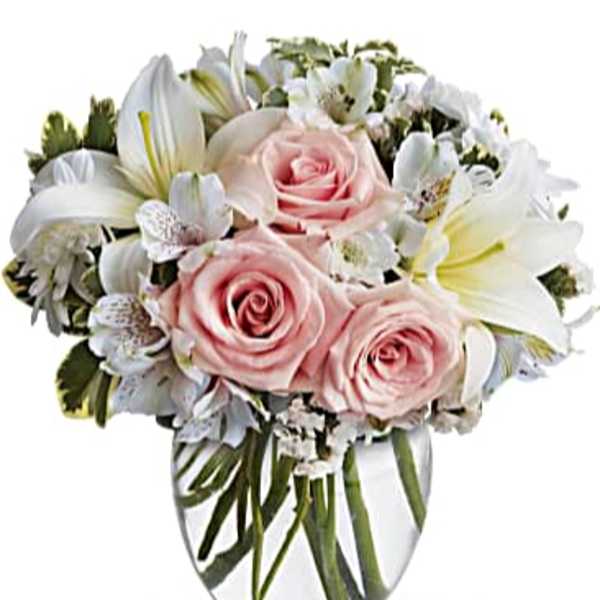 Round glass vase arrangement with pale pink roses, white lilies, and white accent flowers.