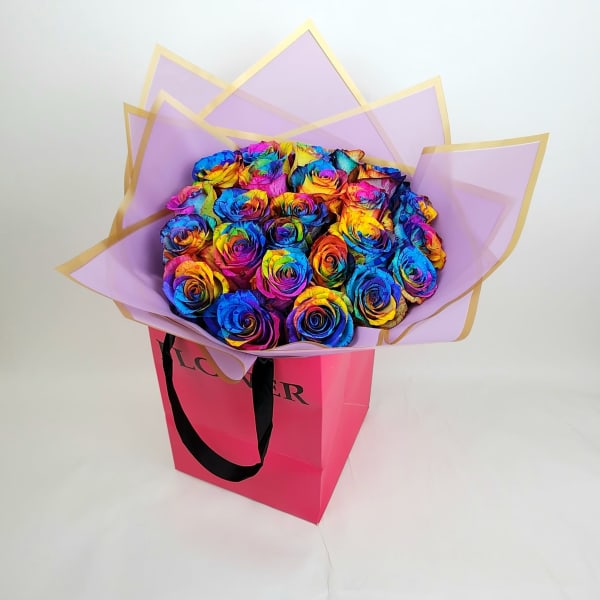 Bouquet of rainbow-colored roses in lavender wrap inside a pink gift bag