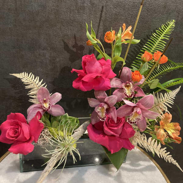 Pink roses and purple orchids arranged in a glass vase with orange accents