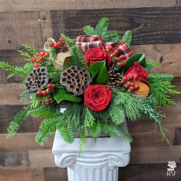 Red roses with pine, berries, and plaid ribbon in a white pedestal vase