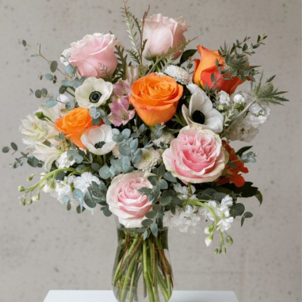 Mixed bouquet of pink and orange roses with white anemones in a clear glass vase
