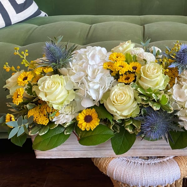 Low floral centerpiece with white roses, hydrangeas, and yellow blooms in a wooden box