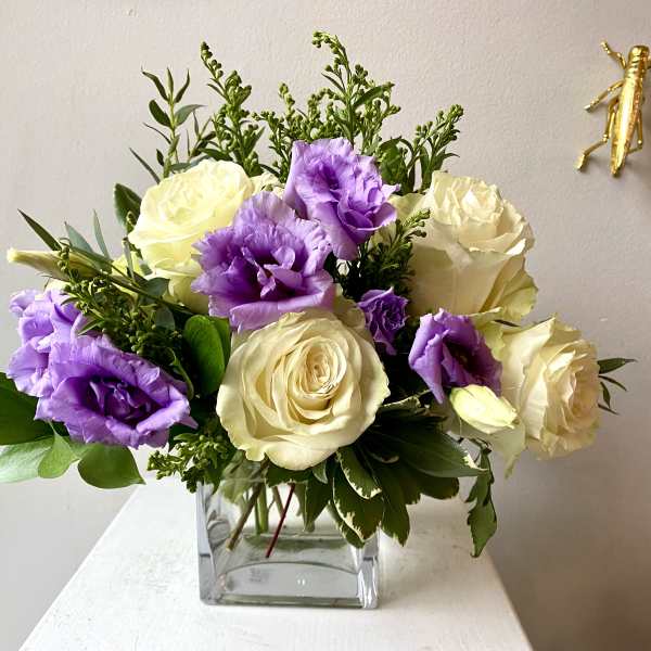 Bouquet of cream roses and purple lisianthus in a clear square vase