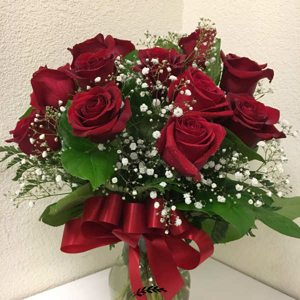 Arrangement of red roses and white filler flowers in a clear glass vase with a red bow