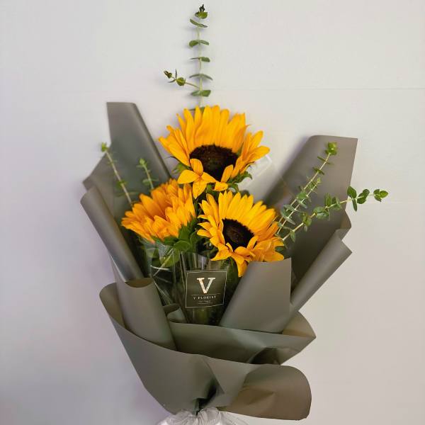 Bouquet of yellow sunflowers with tall eucalyptus stems wrapped in dark paper with a white ribbon bow