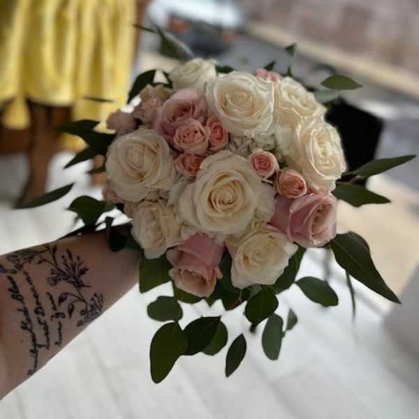 Handheld bouquet of white and blush roses with greenery
