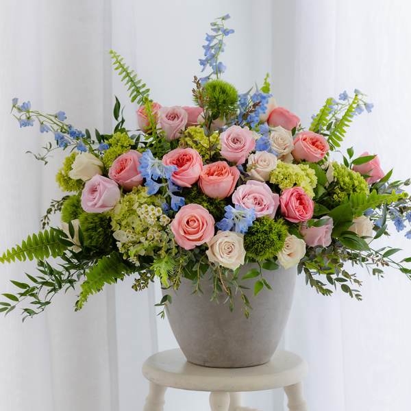 Low gray pot of pink roses, green hydrangeas, and blue delphinium arranged wide on a stool