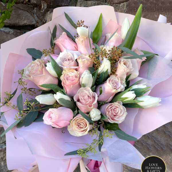 Hand-tied bouquet of pale pink roses and white tulips wrapped in layers of soft pink paper.