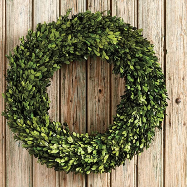 A round green wreath made of dense foliage on a wooden background.