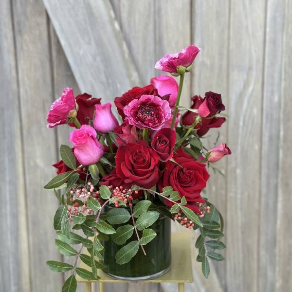 Red and pink roses arranged in a glass vase with trailing greenery.